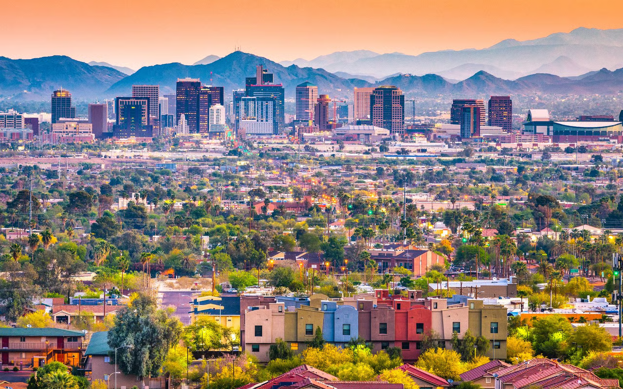 Aerial cityscape view with colorful residential neighborhoods, downtown skyline, and mountain backdrop at sunset